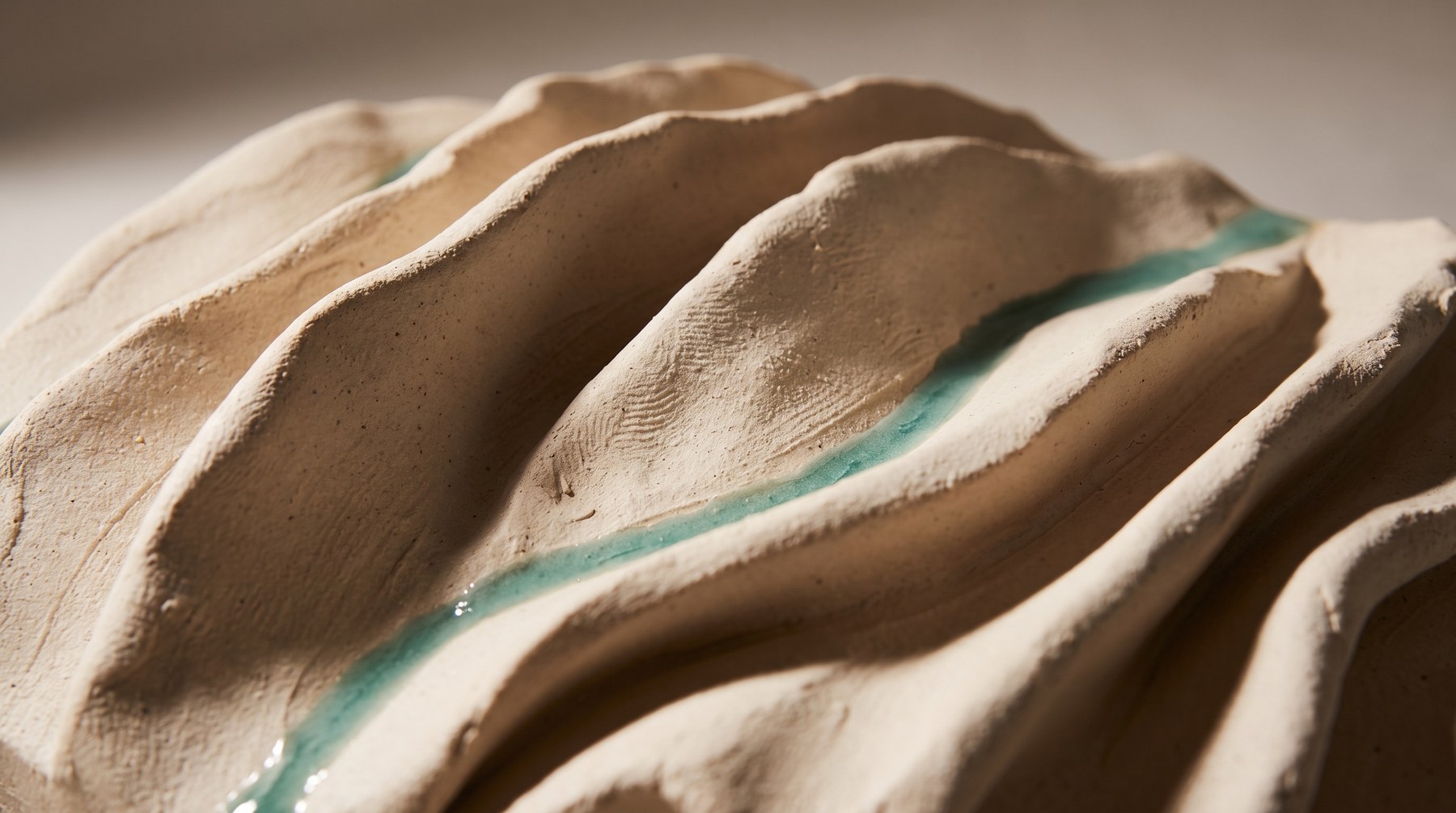 A relief of rolling clay ridges and valleys with a thread of sea-glass glaze pooled in the deepest hollow